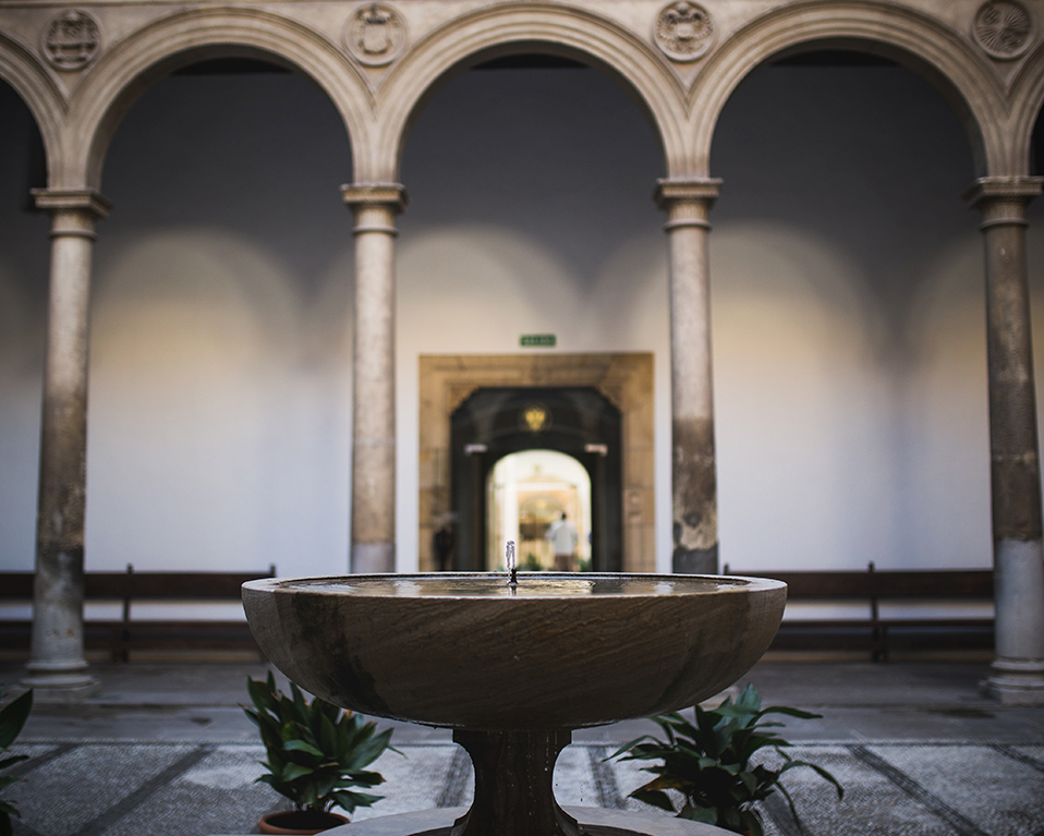 Fuente ornamental central de uno de los patios del Hospital Real con los arcos de columnas al fondo